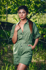 young attractive girl is posing in a forest in the middle of grass and trees on a clear sunny day, portrait