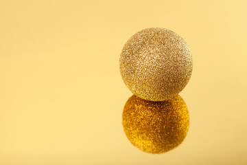 Sparkling golden christmas ball on golden mirror background, selective focus. New year composition.