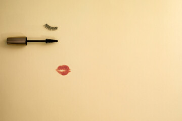 False eyelashes and a mascara wand with a red lipstick kiss mark on an orange background, with copy space.