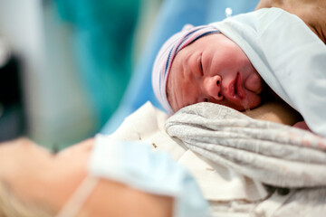 Obraz na płótnie Canvas Newborn baby boy laying down on mother's breast. Mother wears mask.