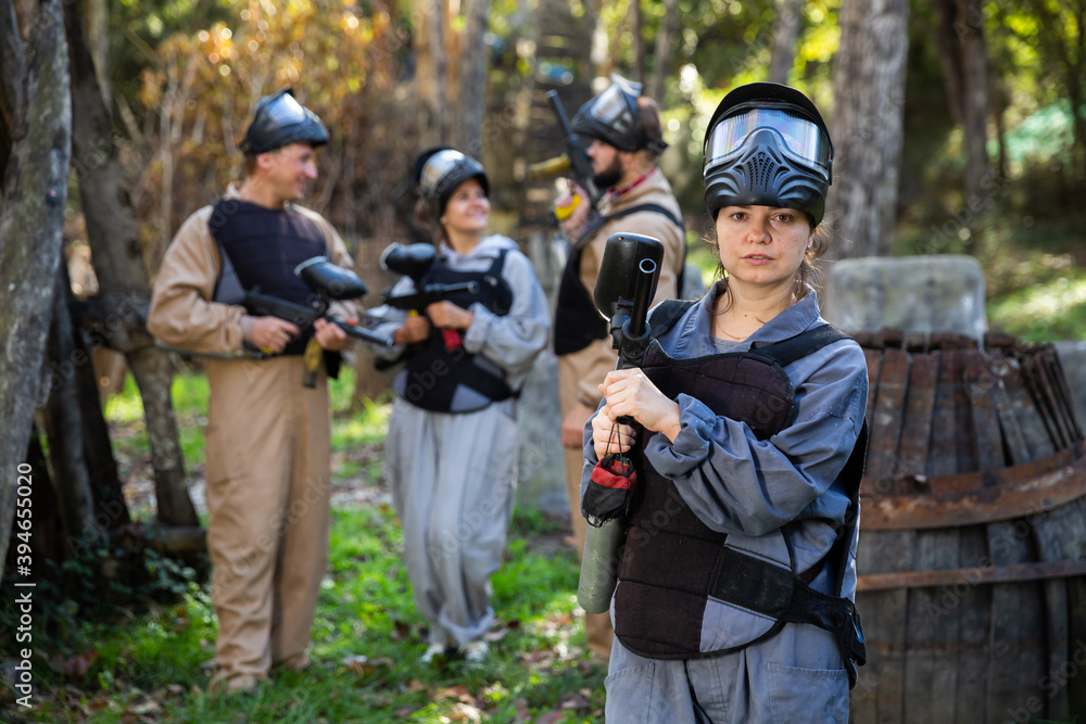 Sticker Female paintball player in camouflage standing with gun before playing outdoors