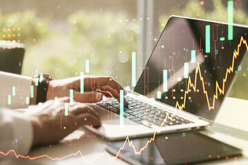 Abstract creative financial graph with hand typing on laptop on background, forex and investment concept. Multiexposure