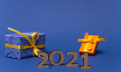 Inscription 2021 and gift boxes with color paper with polka dots tied yellow ribbon on blue background. Christmas and New Year card, banner, advertising concept.