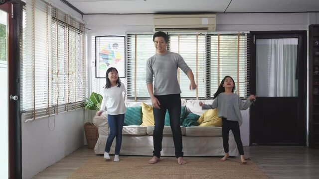 Asian family dancing together in living room at home. Father and daughter enjoyment with music while being celebration at home. Leisure activity stay at home of happy family.