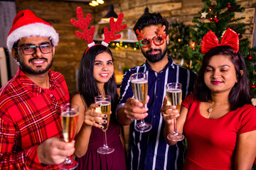 group of four indian friends cheering with champagne flutes and looking happy while having party on the kitchen at stay home quarantine corona virus outbreak party