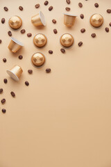 Caffeine, hot drinks and objects concept - close up of golden capsules or pods for coffee mashine with some roasted grains on beige background. Top view with space for text. Flat lay..