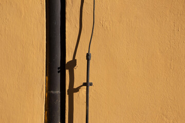 Brown metal downpipe and lightning rod casting shadows on a orange colored wall