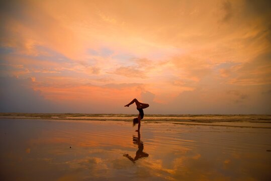 Silhouette Teenage Girl Doing Handstand At Beach Against Cloudy Sky During Sunset