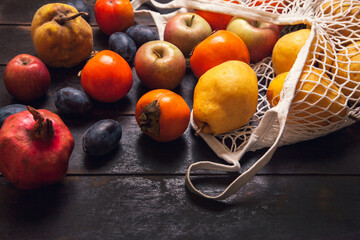 Various autumn fruits in a mesh bag on a dark wooden background