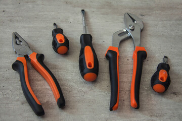 Construction and repair tools. Set on a wooden background. Metal screwdrivers and pliers with black and orange handles. Equipment for electrician, plumber and installer