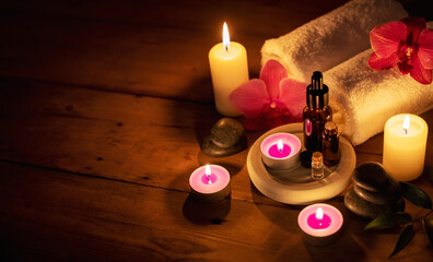 romantic spa - essential oils with massage stones and flowers in cadlelight on wooden background with copy space