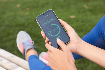 Young woman using fitness app on smartphone outdoors, closeup