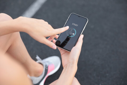 Young woman using fitness app on smartphone at stadium, closeup