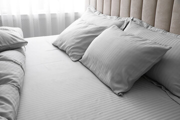 Comfortable bed with soft blanket and pillows indoors, closeup