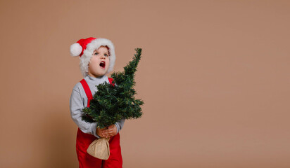 Funny toddler boy holds a Christmas tree and calls Santa, sale in isolation against the background of the trendy color Set Sail Champagne. Holidays, traditions concept.