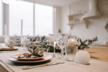 New Year's table setting in a bright kitchen. Glasses, candle, plate with decoration close up. Bright kitchen