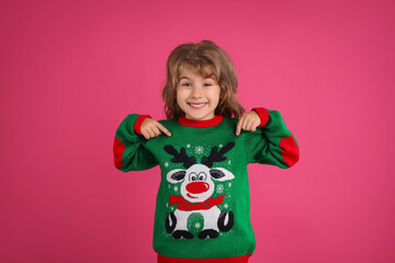 Cute little girl pointing at her green Christmas sweater against pink background