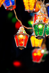 Naklejka premium Wonderful fairy christmas lights with vintage lantern shaped lamps glowing on black vertical background. Colorful garlands for Xmas and New Year winter holiday celebration.