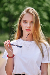 Close-up portrait of a cute teenage girl with long blond hair and sunglasses in hand.
