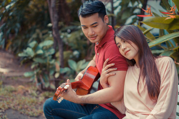 Happy young couple in love sitting in the garden and playing guitar and singing. Concept of Memorable and impressive moments