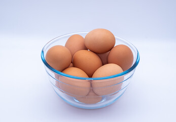 Raw brown eggs in a glass bowl against a white background