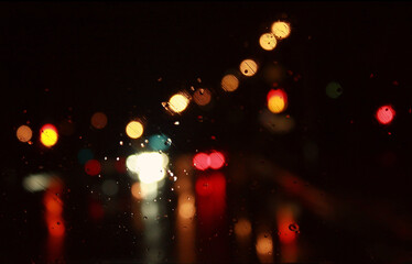 Car traffic lights bokeh through rainy window glass on black background. Defocused city night...
