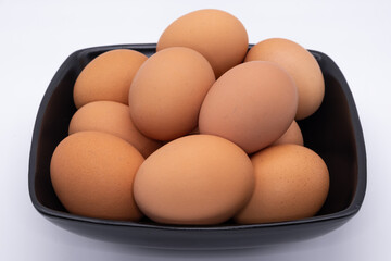 Raw brown eggs on a black plate against a plain white background