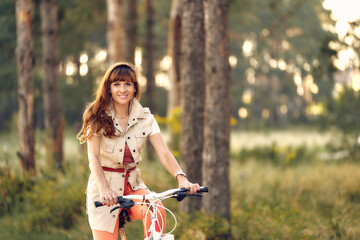 Fototapeta na wymiar A woman in a short dress on nature. Girl rides a bicycle through the forest.