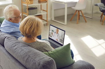 Older couple is sitting at home in the living room and talking to their family doctor via video link