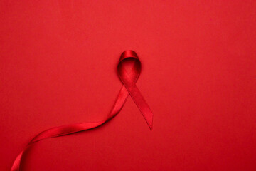 Cancer ribbons. Red ribbon symbol in hiv world day on dark red background. Awareness aids and cancer. Flat lay, top view, copy space - obrazy, fototapety, plakaty