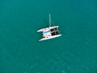 Bird's eyes view of the amazing white catamaran sailing across the blue lagoona. Top view.