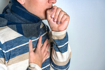 Man feels ill with a sore throat and flu symptoms, coughs into his fist. Space for text on a white background