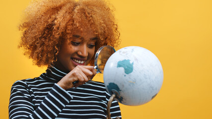 Naklejka premium Happy african american black woman looking at the globe through the magnifier. High quality photo