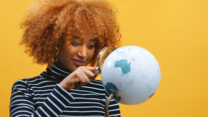 Naklejka premium Young african american black woman looking at the globe through the magnifier. High quality photo