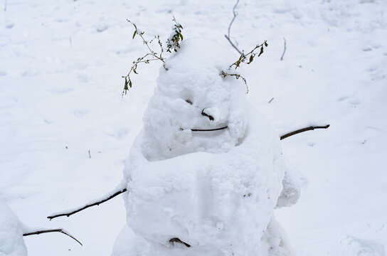 Ugly snowman from the first snow with arms from branches and creepy smile. Children's and family outdoor winter fun. Winter concept