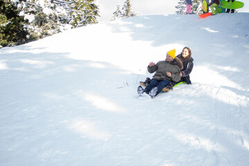 Happy young couple going down a small snowy hill on a sled