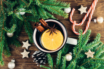 Top view of Christmas and New Years drink hot wine, mulled wine, punch or tea on wooden background next to green tree and Christmas candy canes.
