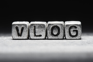 concept of vlog. The inscription on metal 3D cubes isolated on a black background, grunge style