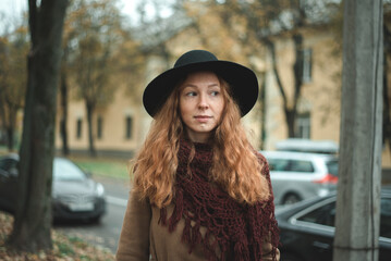Girl with red hair in a black hat and coat in an autumn park