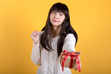 Portrait of lovely asian woman in white sweater holding a gift. valentine's day concept photos. Studio shot isolated on yellow background.