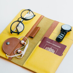Bright yellow opened travel wallet for documents. Inside passport or id card, boarding pass and money. Near black glasses, hand watches and white headphones. Vacation and tourism concept.
