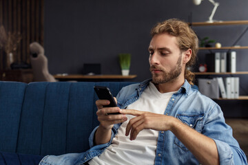 Curvy guy using smartphone and smiling. Happy man using mobile phone apps, texting message, browsing internet, looking at smartphone, sitting at home. Young people working with mobile devices.