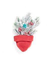 Abstract Christmas composition. The snow-covered spruce branches are decorated with bunches of red berries and are in a pot made of a knitted hat. Flat lay. Top view.