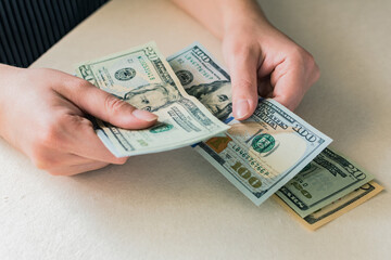 Woman's hands counting dollar bills, on white desk.