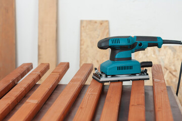 Electric sheet finishing sander on wooden slats for production of  wooden garden bench on table in carpentry  workshop