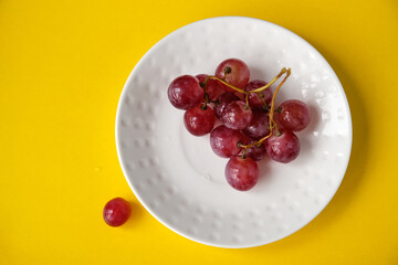 A small bunch of pink grapes lies on a white saucer. Fresh seasonal grapes in plate ready to eat On yellow background. Healthy food.