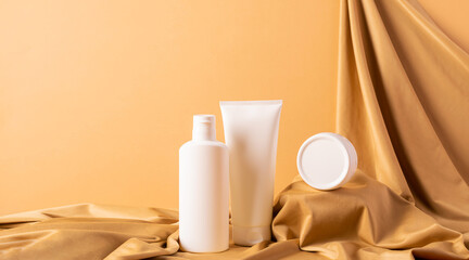 Group of cosmetics tubes bottles abstract podium yellow background draped cloth.