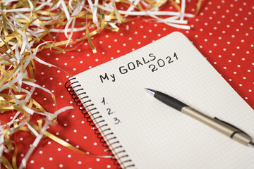 Phrase My Goals 2021 in a notebook, black pen. Red background and tinsel. New Years concept