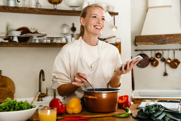 Beautiful woman smiling and using cellphone while making lunch