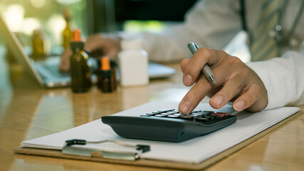Medical hand holding pen and pressing calculator Use the notebook at your desk in the clinic with the vial in the background.